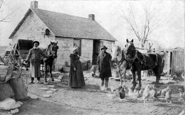 People standing in front of a small home in Dunlap, Kansas holding horses and with chickens in the foreground