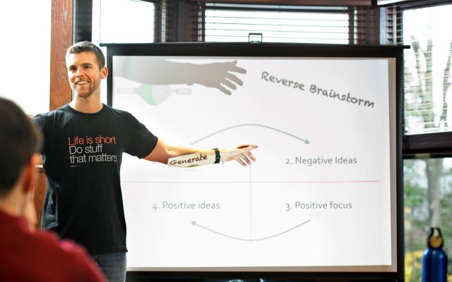 Man smiling and standing in front of a projection screen and pointing to text