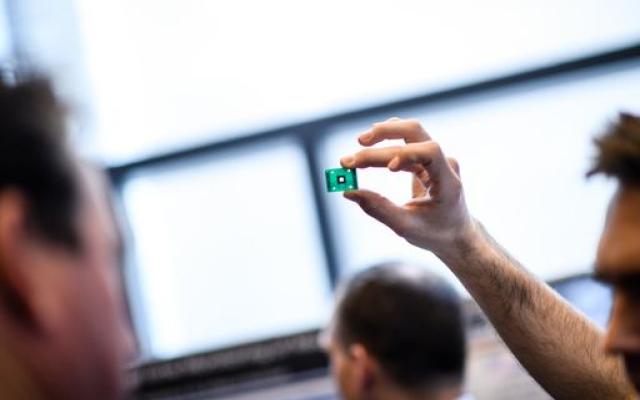 student holding a computer chip up to the sun light of a wide window