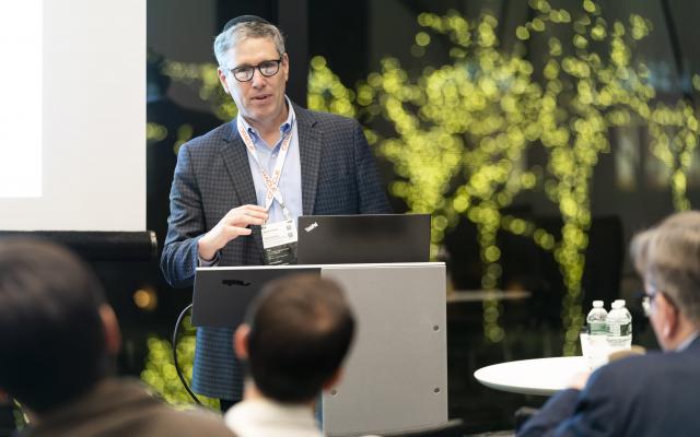 Man with glasses presenting at podium with green background