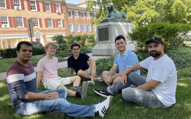 Five students sitting on the grass in front of a tiger statue.