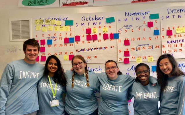 Tiger Challenge students wearing matching shirts standing in front of a wall filled with posters and sticky notes