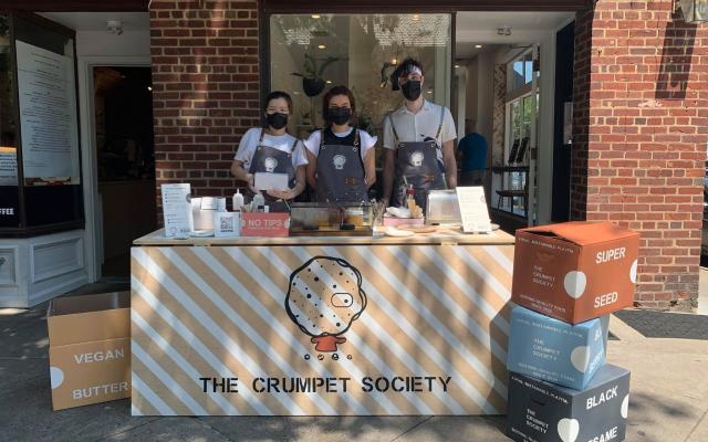 Three students selling crumpets at a pop-up restaurant on the sidewalk in front of a cafe