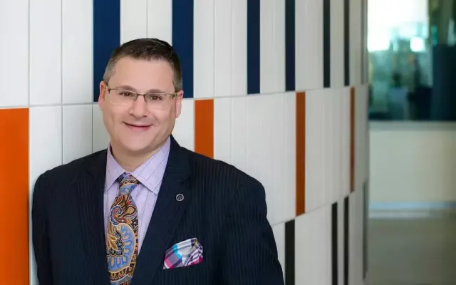 David Postolski standing in a suit in front of a wall with colored squares