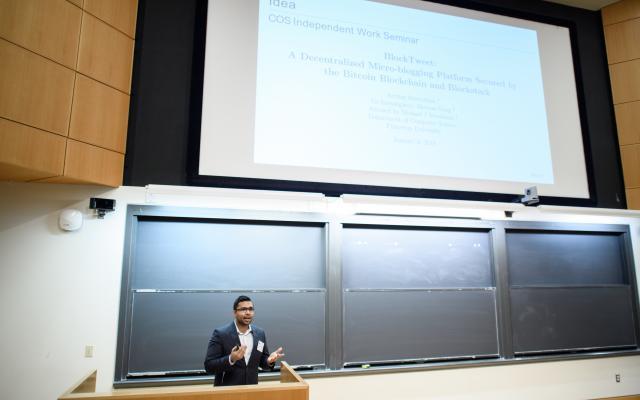 A person presenting from podium with a large slide projected overhead