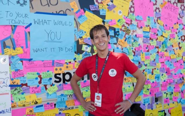 Man in red t-shirt wearing lanyard in front of wall of post-its