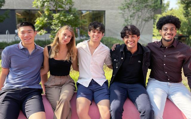 Five students outside sitting on a wall together