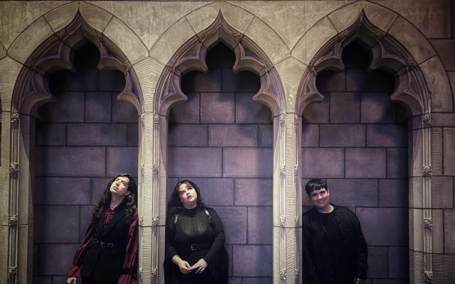 Team members stand in darkly lit individual chapel alcoves wearing gothic attire