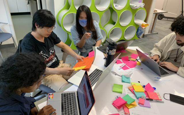 three students and an instructor discussing a project in front of a table full of colored sticky notes