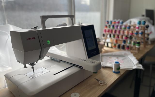 An embroidery machine sitting by a window with a rack of colourful thread in the background