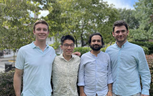 Four smiling young men standing in a park