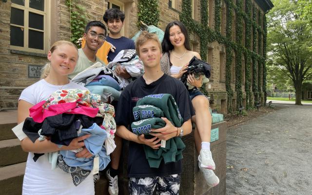 Grace Anne McCooey, Nadula Gardiyehewa, ayushmaan Kher, Vivian Chang, and Sergei Kudriavtcev standing outside Nassau Hall holding piles of clothing