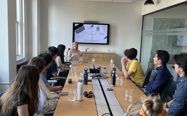 Genevieve Bellaire presenting to a long conference table full of students 