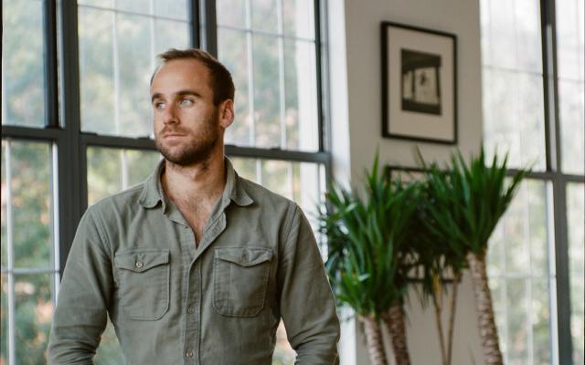 Man in green shirt standing in front of windows and plants