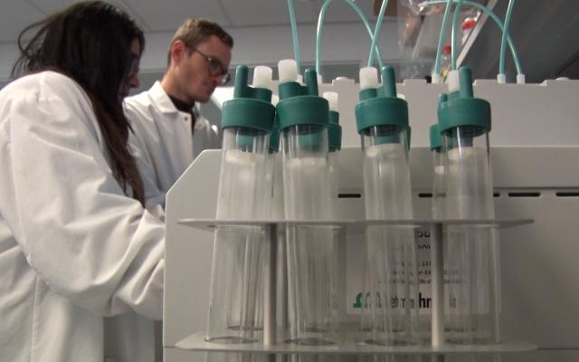 Two people in lab coats in the background a bank of test tube in the foreground