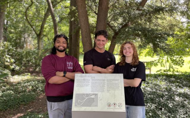 Three students standing around a plaque acknowledging the Native lands Princeton is built on.