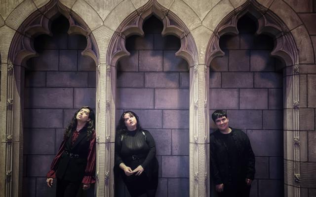 Three students standing in gothic alcoves that are drenched in purple light
