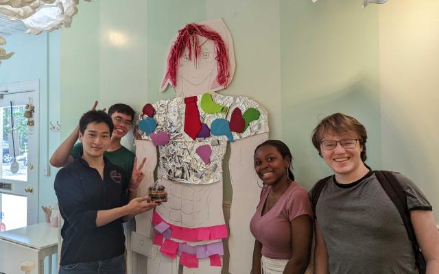 Smiling students standing in a cafe with an 8 foot tall cardboard cutout of a student