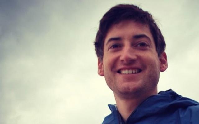 Man with blue jacket in front of clouds