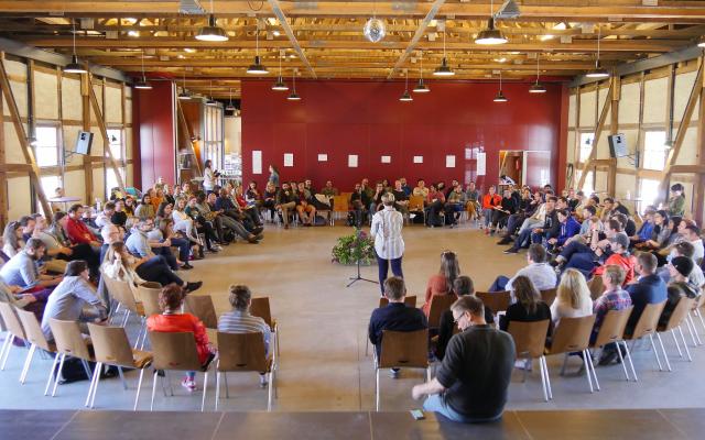 A person presenting to a crowd of people surrounding them in a circle