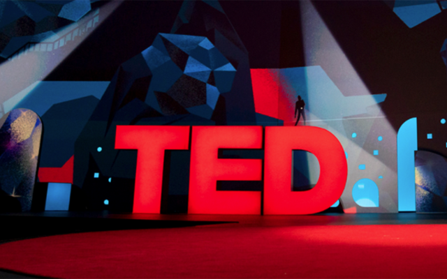 Iconic TED talk stage with red rug and red TED letters in background