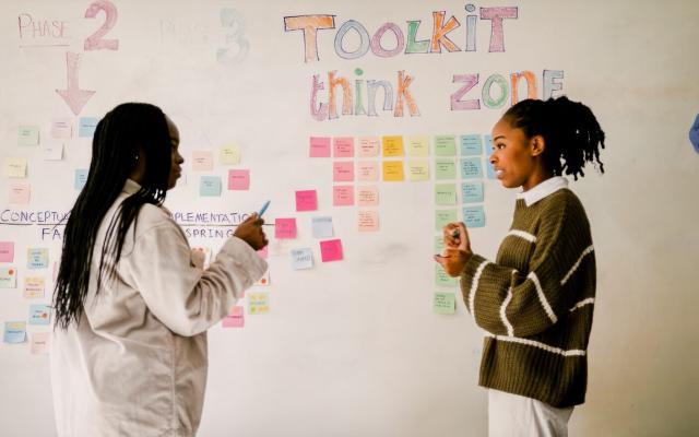 Two students in front of a whiteboard wall with post it notes