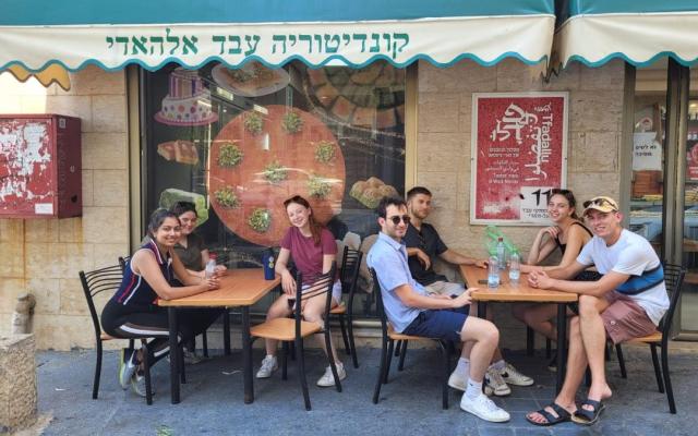 Seven casually dressed students sitting at outdoor tables at an establishment in Haifa, Israel