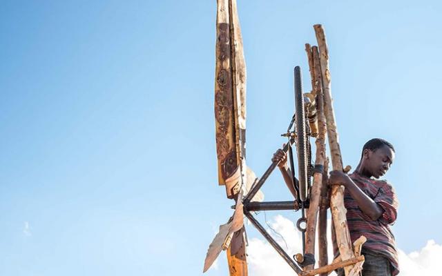 William Kamkwamba standing on wooden structure with sky in background