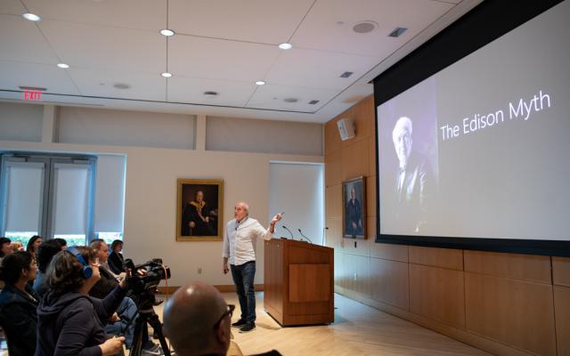 Bill Buxton talking to an audience in front of a podium with a slide projected on a screen