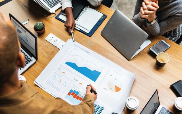 Three individuals with laptops point at graph on table