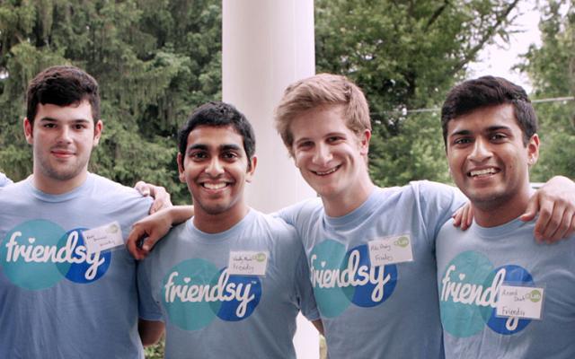 Four smiling males in gray shirts with their arms around each other