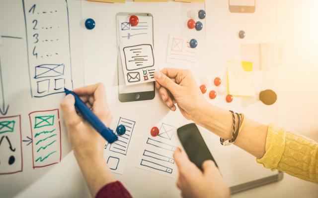 Hands drawing and pasting low fidelity wireframe design elements on a whiteboard