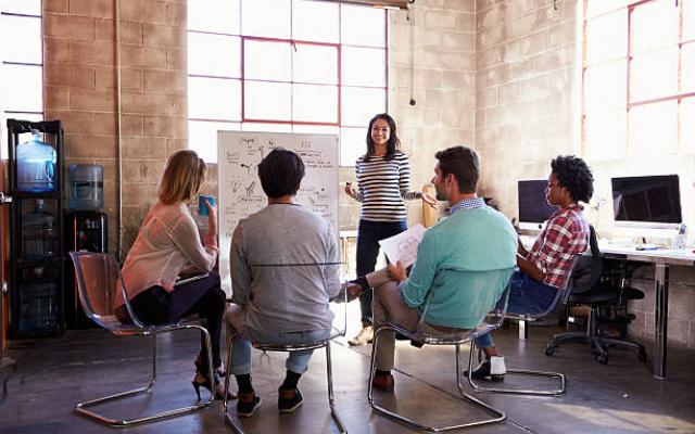 Woman in striped shirt presenting to four colleagues