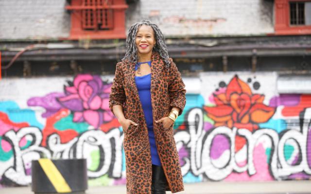 Majora Carter wearing long brown leopard jacket standing in front of a colorful outdoor background