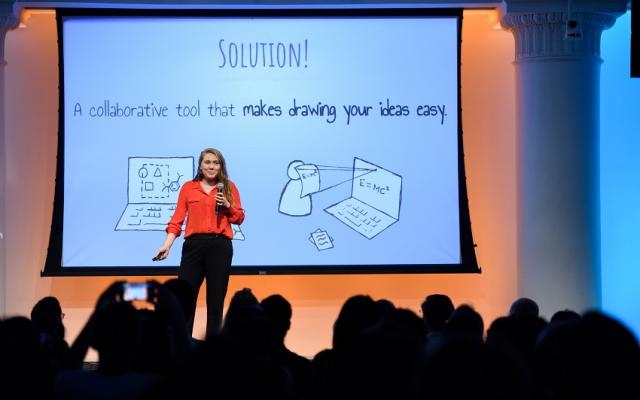 Female standing in front of a screen presenting to a seated crowded