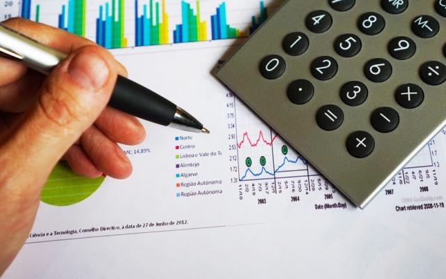 Hand holding pen with calculator and graphs