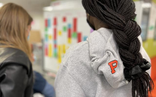 back of two women students working at a whiteboard one in a Princeton University hoodie