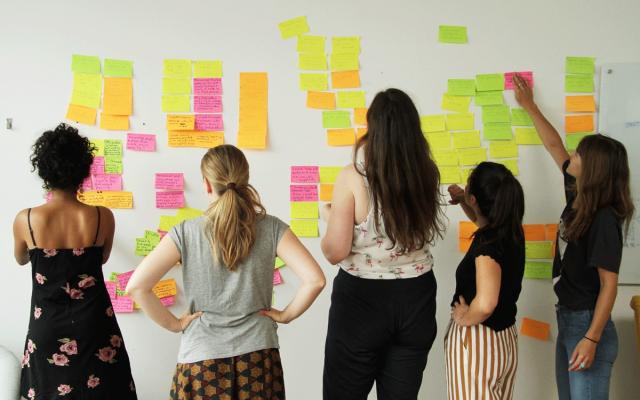 5 students with back to the camera putting post-its on a wall