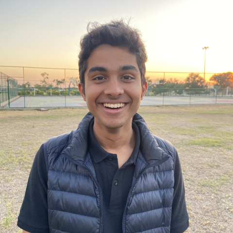 Saarthak smiling in front of sunset and tennis court 