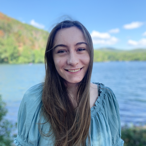 Student smiling outside near water and hills