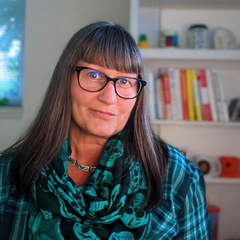 woman with long hair, wearing glasses and turquoise scarf and shirt, smiling