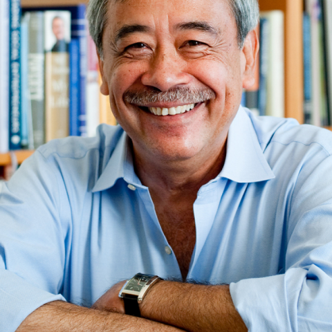 photo of a man with a mustache sitting in front of a bookshelf